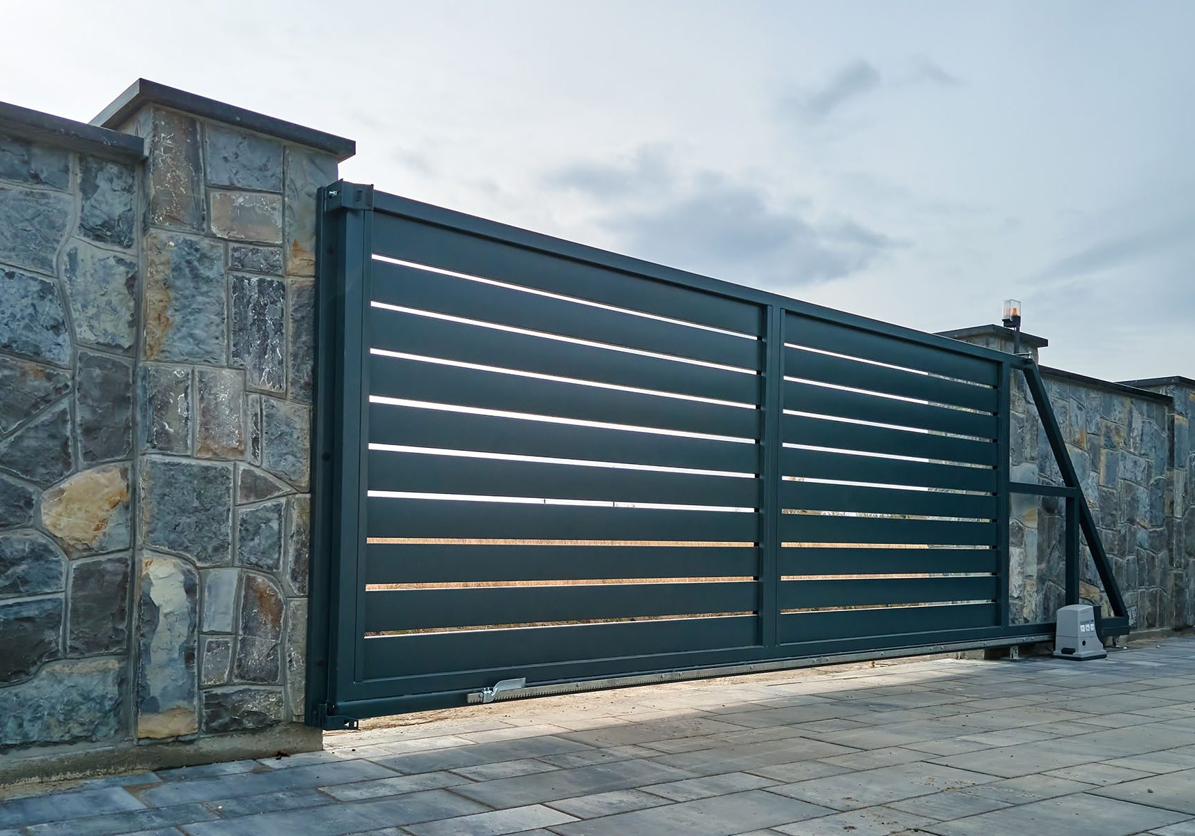 Wide automatic sliding gate with remote control installed in high stone fense wall. Security and protection concept